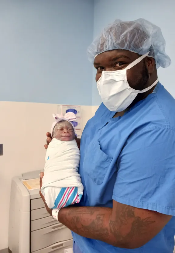 a man in scrubs holding a baby in a hospital room