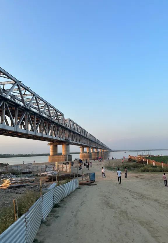 people walking on a beach under a bridge