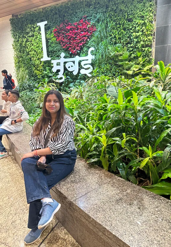 a woman sitting on a bench in front of a plant wall