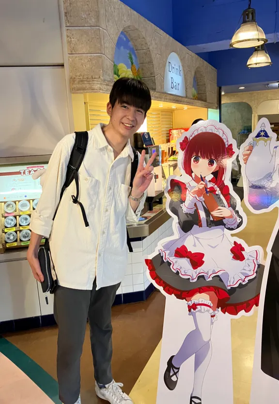 a man stands next to a cardboard cutout of an anime character. He's not sure if it's supposed to be a character from a popular anime series, or just an anime character in general. make it a real person