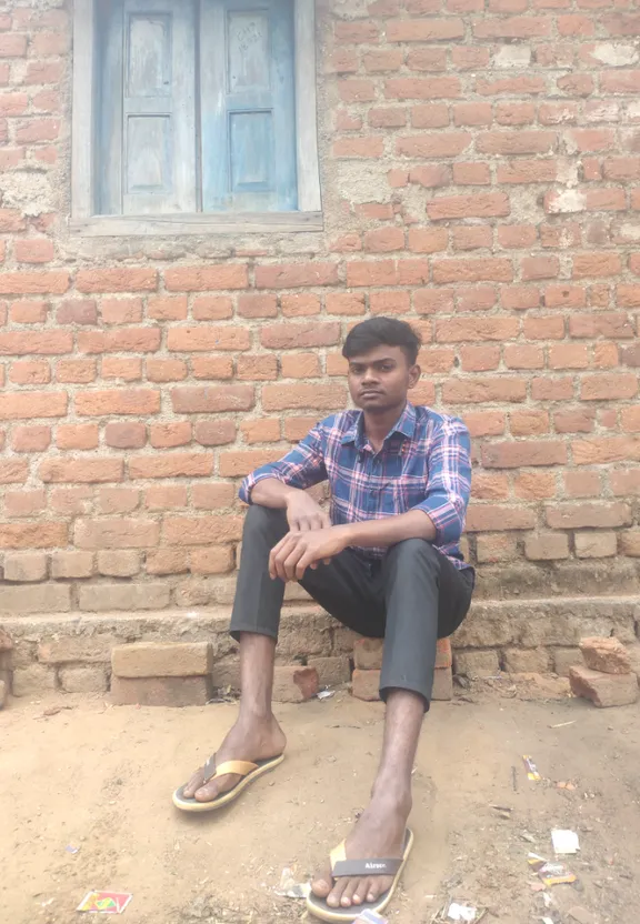 A man sitting in front of a brick building. Add a tree in the background.