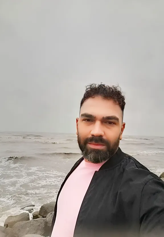 a man with a beard wearing a pink shirt and black jacket