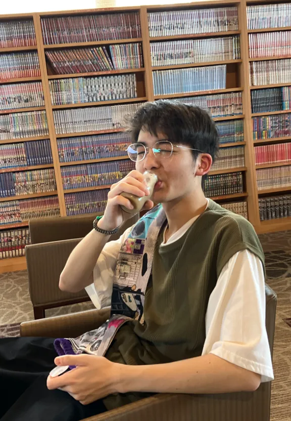 a young man sitting in a chair in front of a book shelf