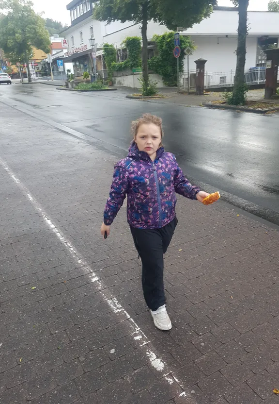 a little girl walking down a street holding an orange