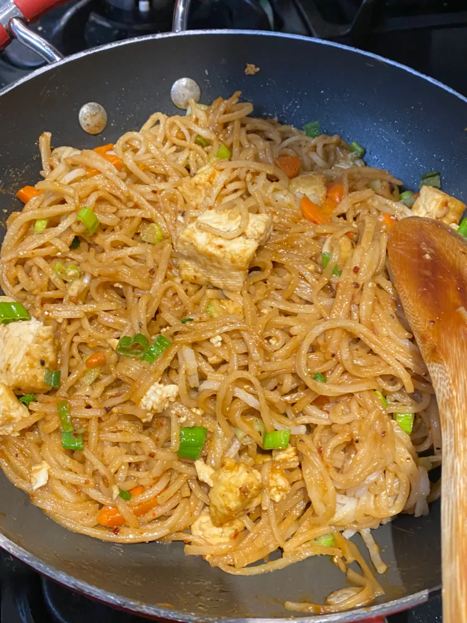 a wok with noodles and vegetables cooking on the stove