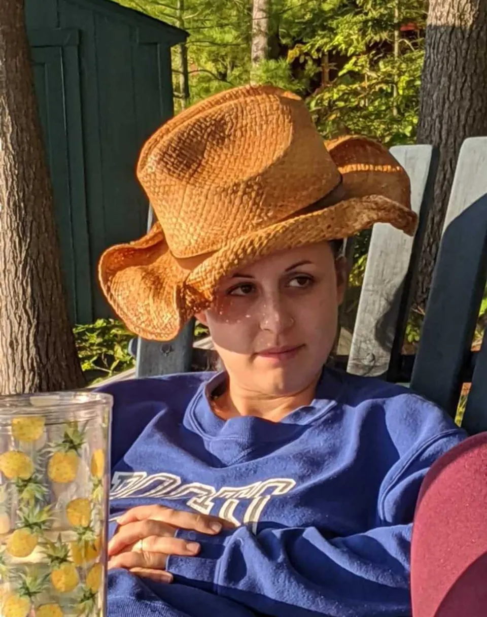 a woman sitting in a chair with a straw hat on her head opens her mouth and takes a drink