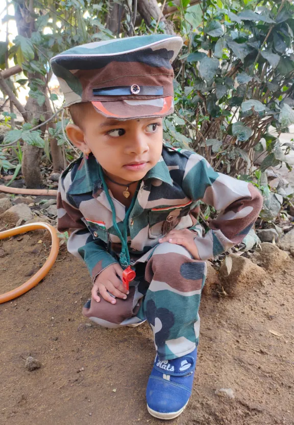 a little boy in a camouflage uniform sitting on the ground