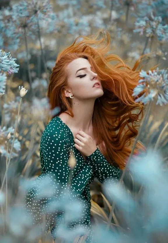 a woman with red hair sitting in a field of flowers