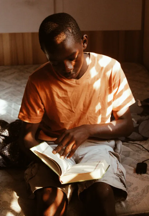 a man sitting on a bed reading a book