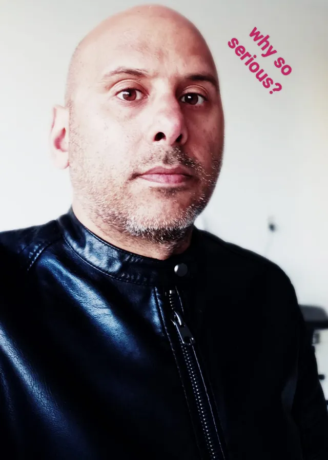 a bald man wearing a black leather jacket. forehead, face, eyebrow, beard, mouth, flash photography, jaw, neck, sleeve, collar