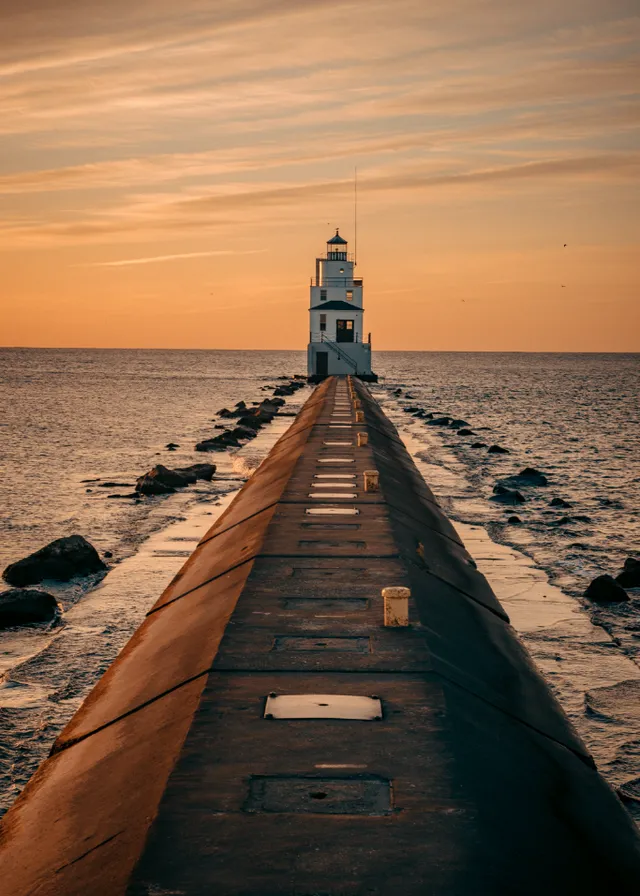 a light house sitting on the end of a pier. water, sky, wood, cloud, afterglow, sunlight, horizon, dusk, sunset, sunrise