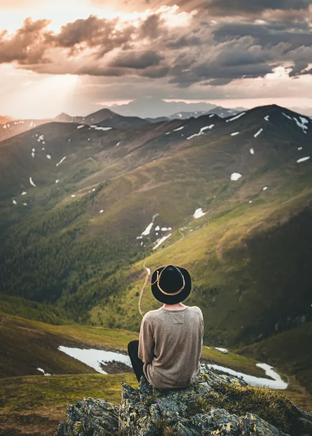 a person sitting on top of a mountain. cloud, sky, mountain, people in nature, light, nature, highland, plant, happy, sunlight