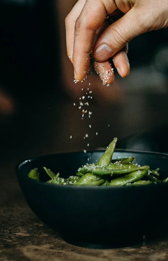 a person sprinkling salt on a bowl of green beans. food, ingredient, recipe, liquid, gesture, cuisine, dish, cooking, nail, drink : 2 | blurry, ugly, deformed, jpeg, low resolution : -1