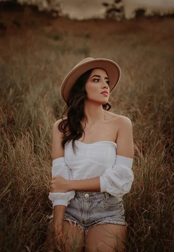 a woman sitting in a field wearing a hat