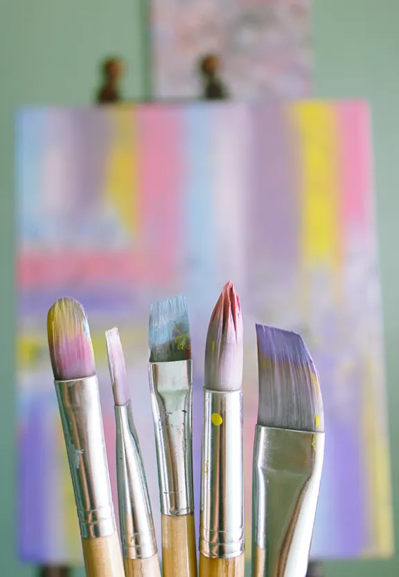 a group of paint brushes in front of an easel