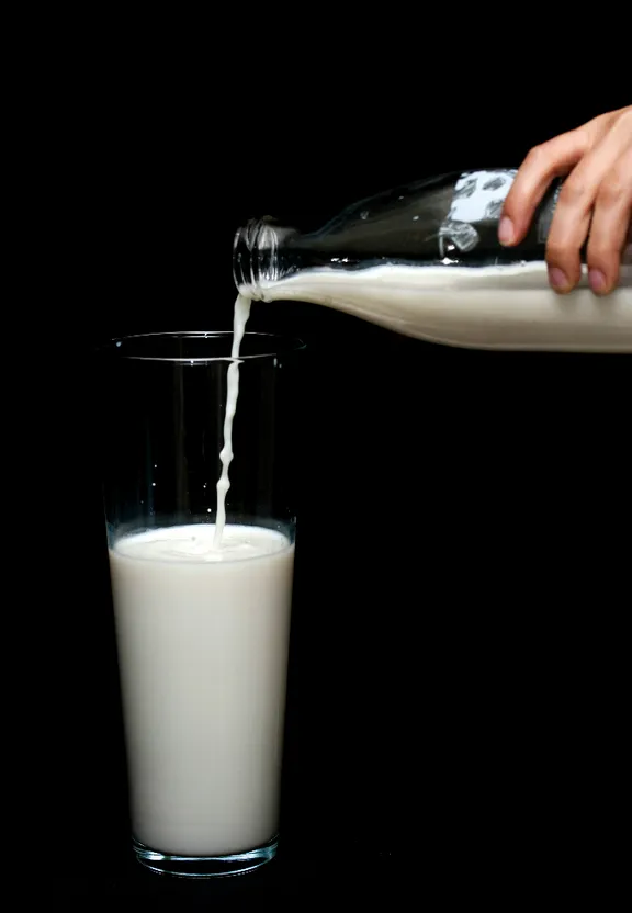 In a modern kitchen, the milk is being poured into a glass by a person in a chef's hat