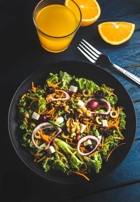 a black plate topped with a salad next to a glass of orange juice