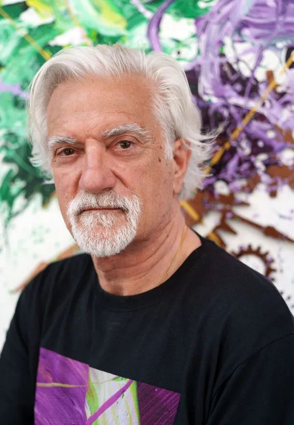 a man with white hair and a black shirt in front of a painting