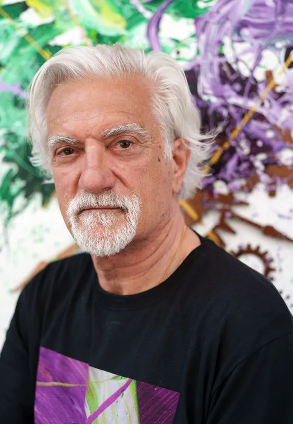 a man with white hair and a black shirt in front of a painting