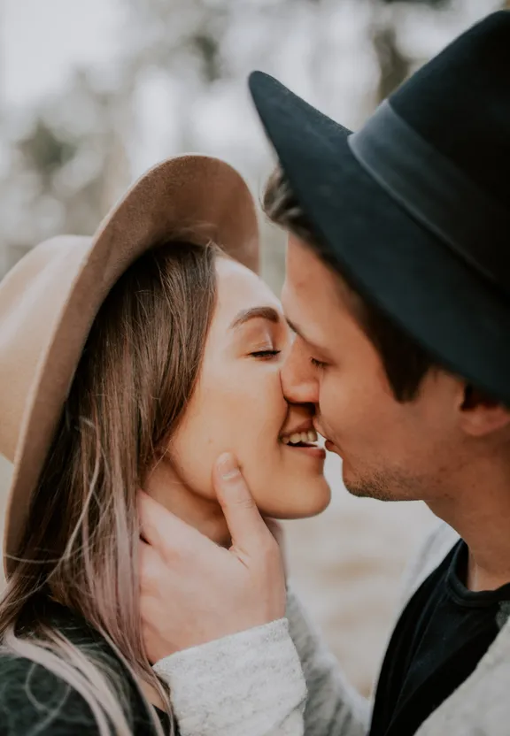 a man kissing a woman's face with a hat on
