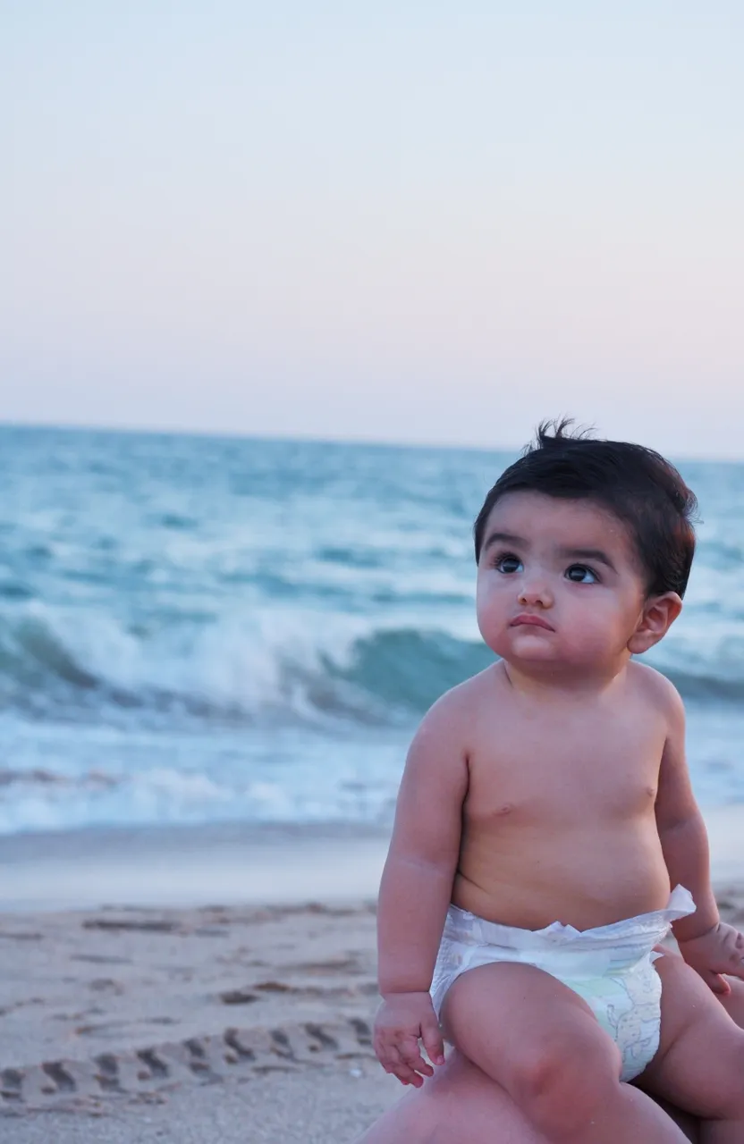 a baby in a diaper sitting on the beach