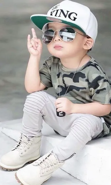 a little boy sitting on a ledge wearing a hat and sunglasses