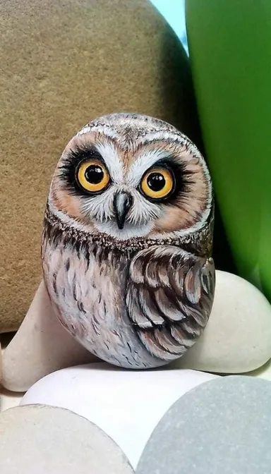 an owl figurine sitting on top of a pile of rocks. bird, head, owl, beak, bird of prey, screech owl, artifact, feather, art, barn owl