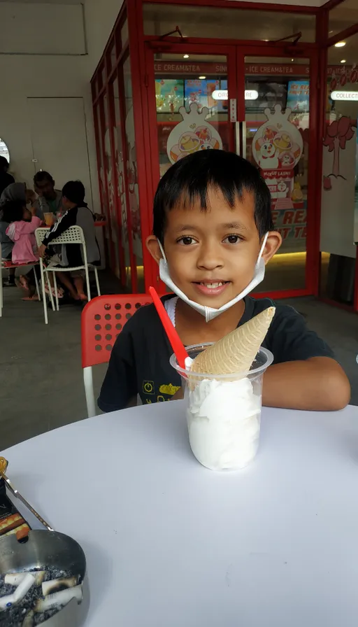 a young boy sitting at a table with a banana and milkshake