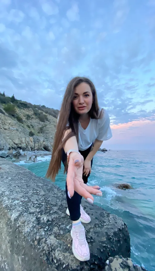 a girl is posing on a rock near the ocean