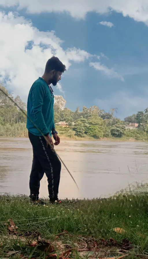 a man with a fishing pole standing on the bank of a river