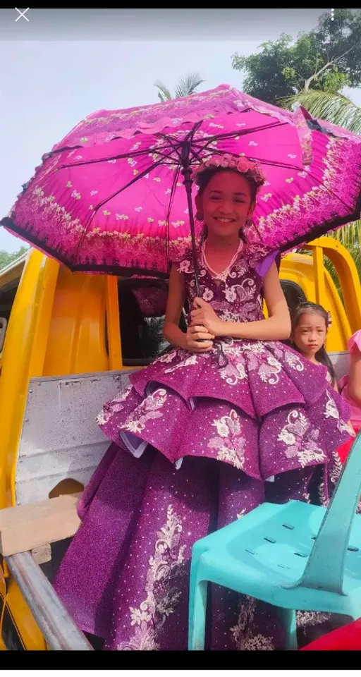 a little girl sitting in the back of a truck holding an umbrella