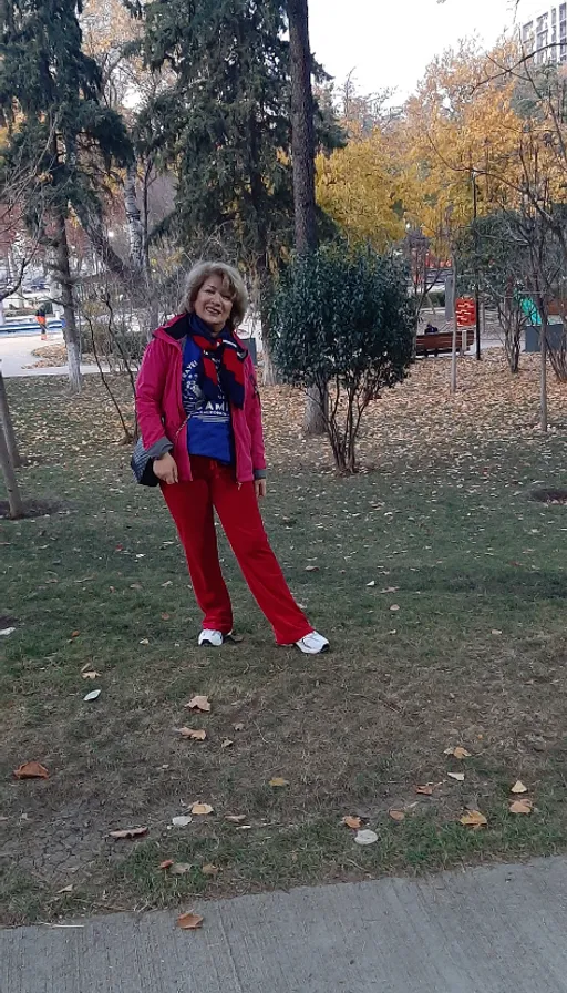 a woman standing in a park with a frisbee. plant, tree, people in nature, branch, grass, leisure, recreation, electric blue, deciduous, human leg