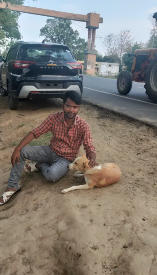 a man kneeling down next to a dog on a dirt road