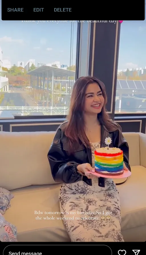 a woman sitting on a couch holding a rainbow cake