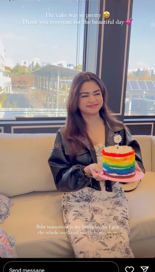 a woman sitting on a couch holding a rainbow cake