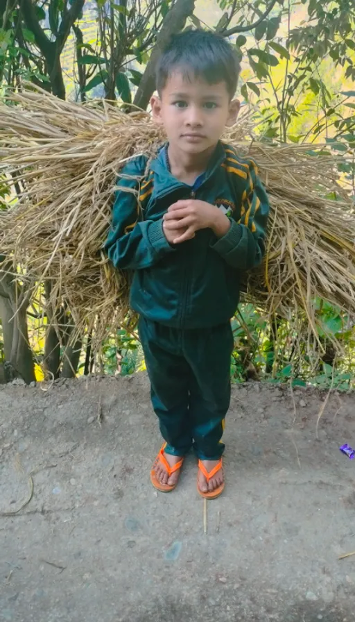 a young boy standing in front of a pile of hay