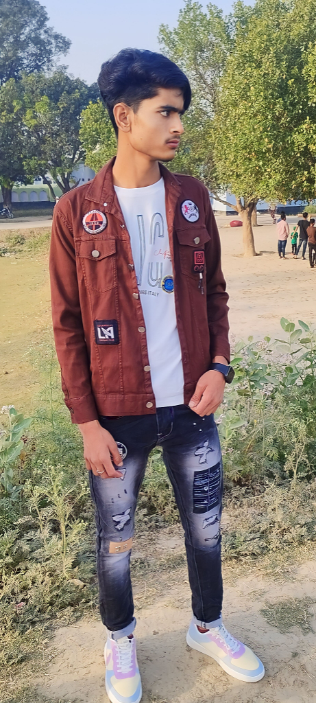 a young man standing in a park wearing a jacket and jeans