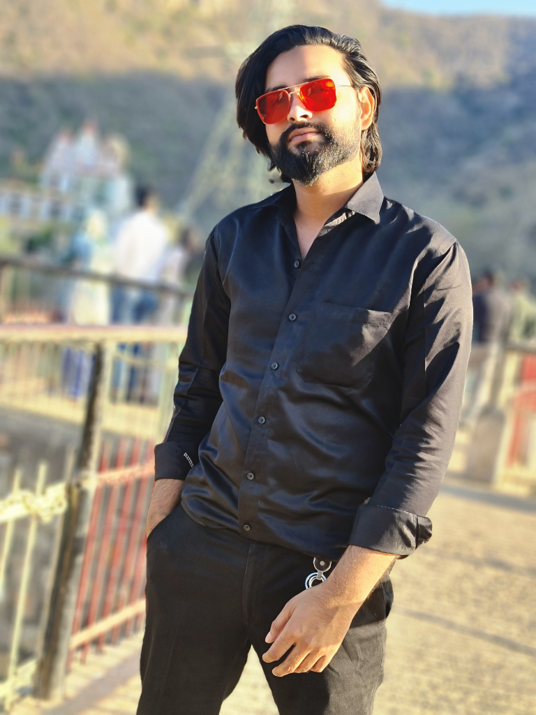 a man with a beard and sunglasses standing in front of a fence