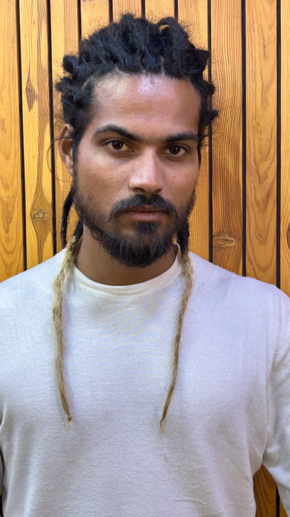 a man with dreadlocks standing in front of a wooden wall