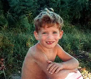 a young boy sitting on a surfboard in the sand