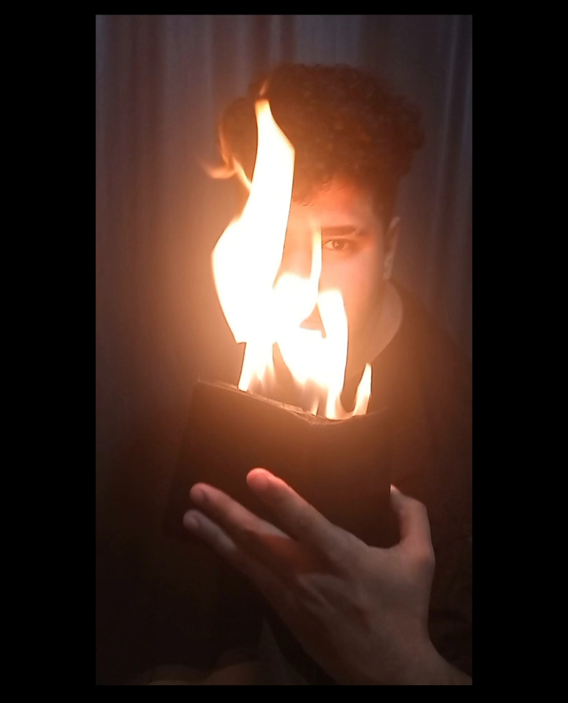 a man holding a book with fire coming out of it. a man holding a book with flames coming out of it
