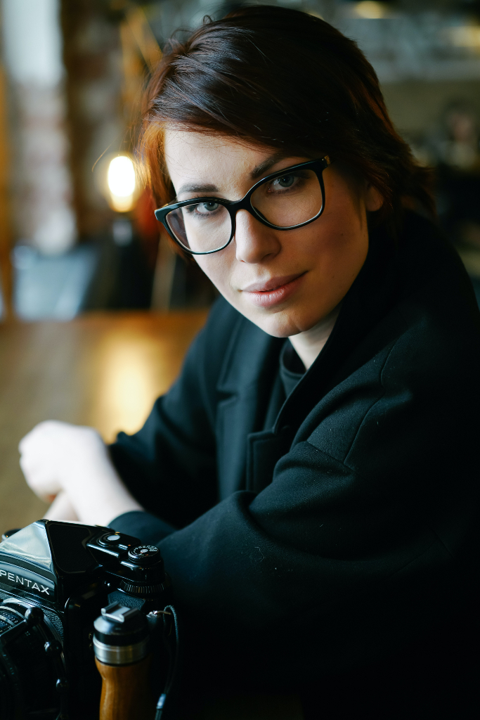 a woman with glasses sitting at a table with a camera