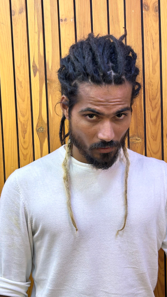 a man with dreadlocks standing in front of a wooden wall