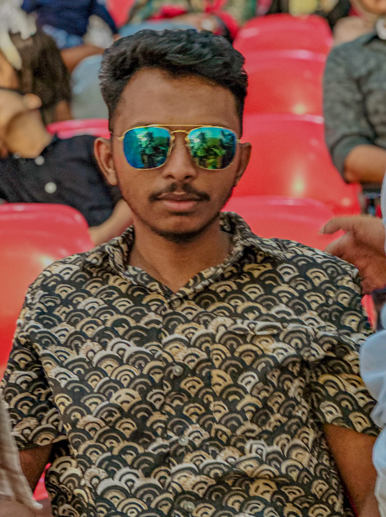 a man wearing sunglasses sitting in a stadium